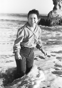 Black and white photo: Gloria Anzaldua standing knee-deep in water at the beach
